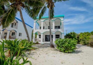 Front view of a beautiful 2-bedroom, 2-bath home for sale in North Ambergris Caye, featuring tropical landscaping and a spacious exterior